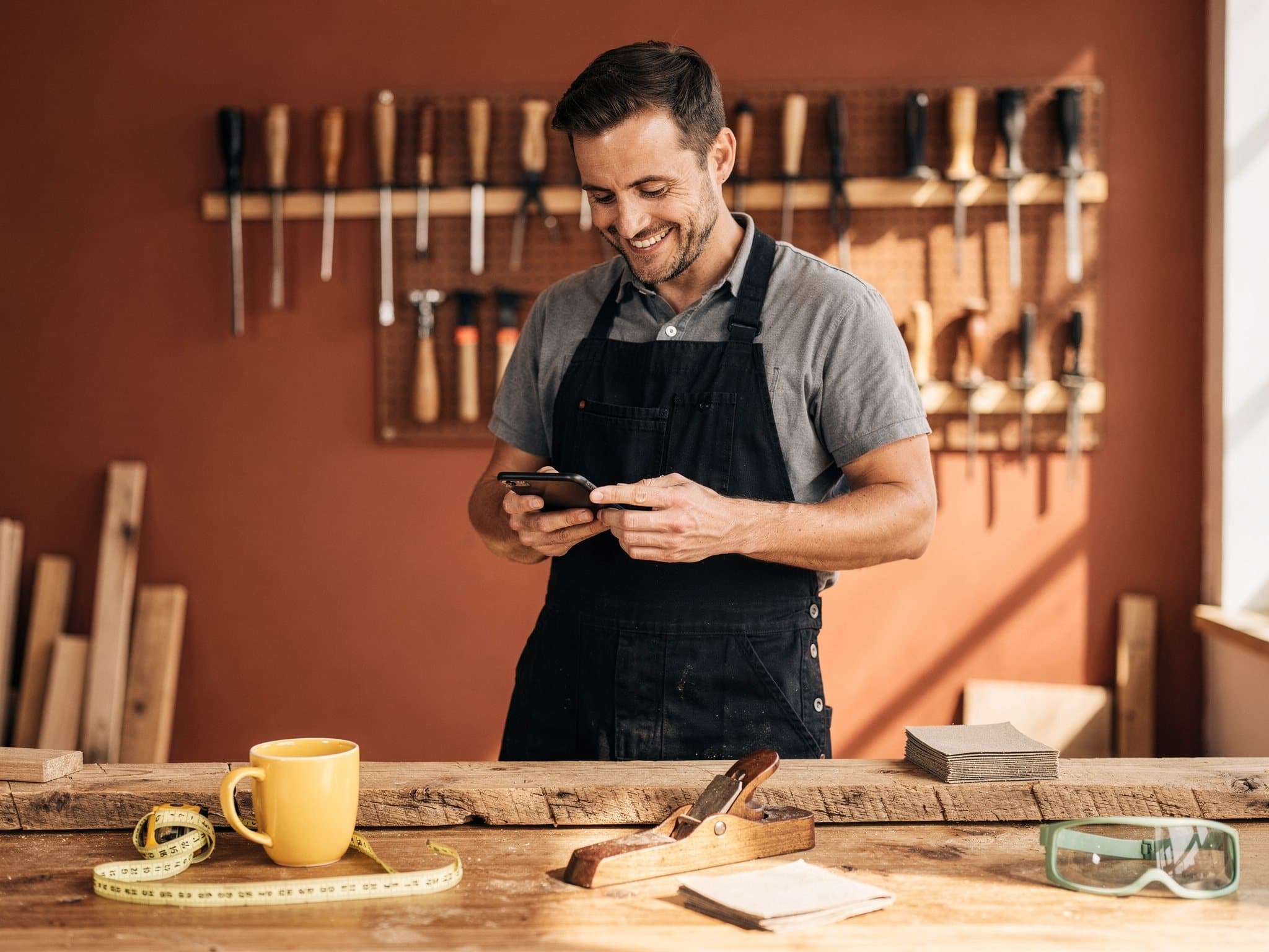 Artisan souriant consultant son téléphone dans son atelier de menuiserie